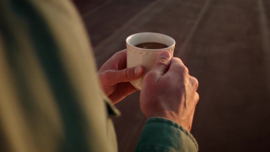 A white man holds a cup of a hot liquid