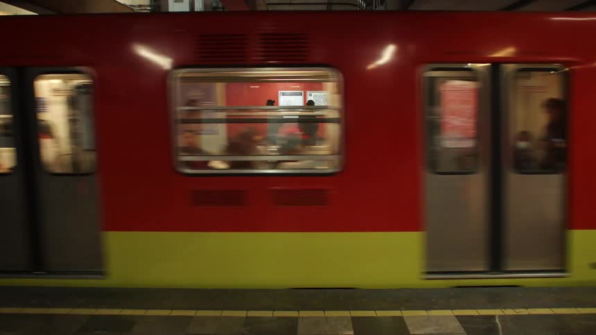 A red and yellow colored train full of people is stopping at a station