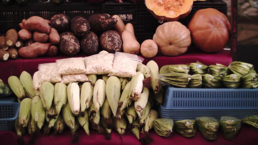 Several people pass by food displayed at an outdoor market
