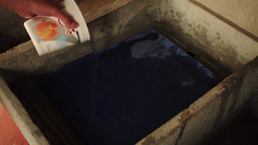 A hand pouring water onto a clothes item in a wash tank