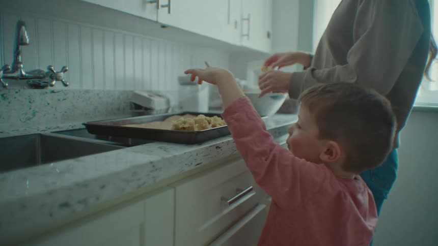 Portrait of a boy helping his mother in the kitchen in preparing small cupcakes