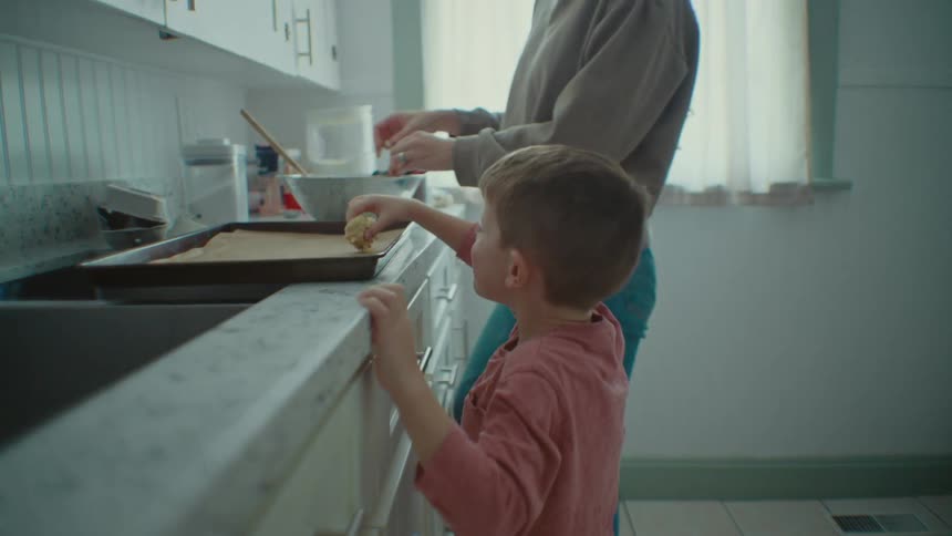 Son helps mom put food in tray in the kitchen