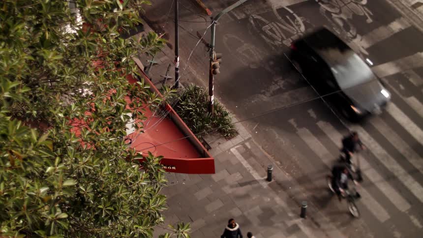 Downward view of pedestrians walking and a street with motorcycles bicycles and vehicles passing by