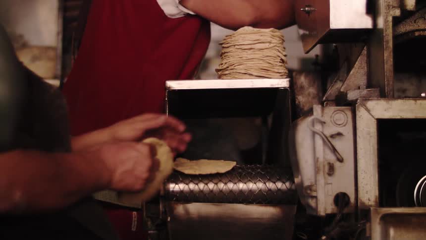 Tortillas being produced by a machine with people overseeing the process