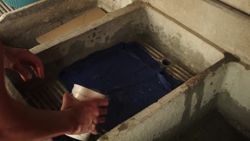 A person washing a blue cloth in a worn concrete basin