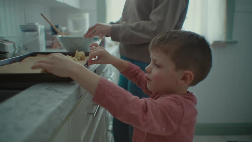 A boy and his mother make cookies in a kitchen