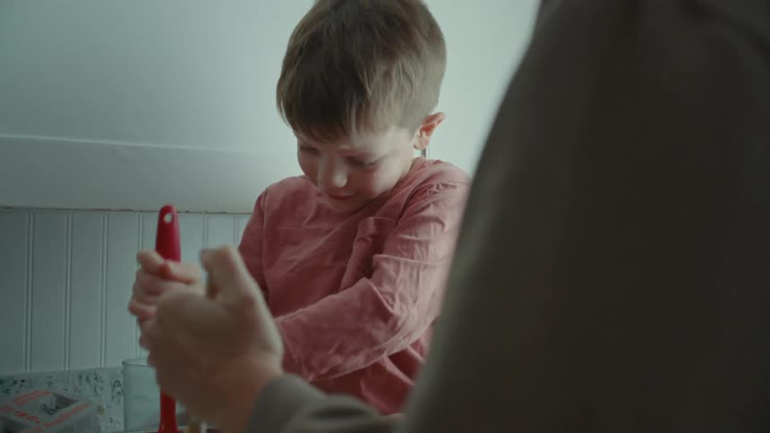 Portrait of a boy helping his mother in the kitchen with a spatula