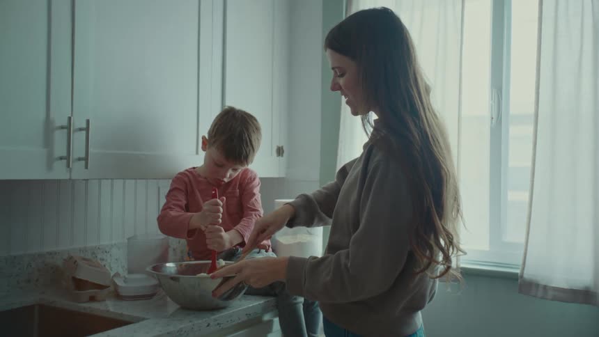 Mother and son mash cookie dough in a silver bowl in the kitchen