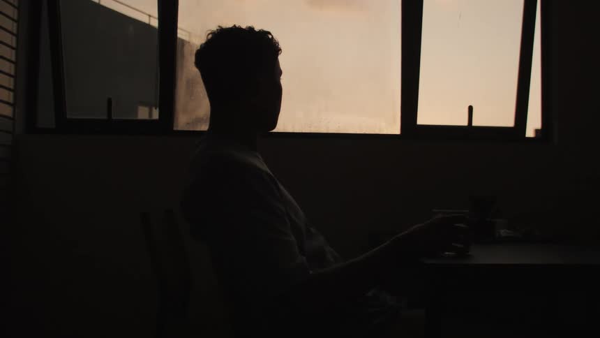Silhouette of a men sitting in the room holding a glass