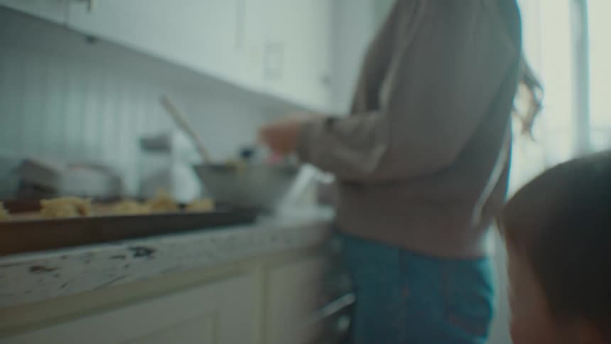 Portrait of a little boy jumping next to his mother who is cooking