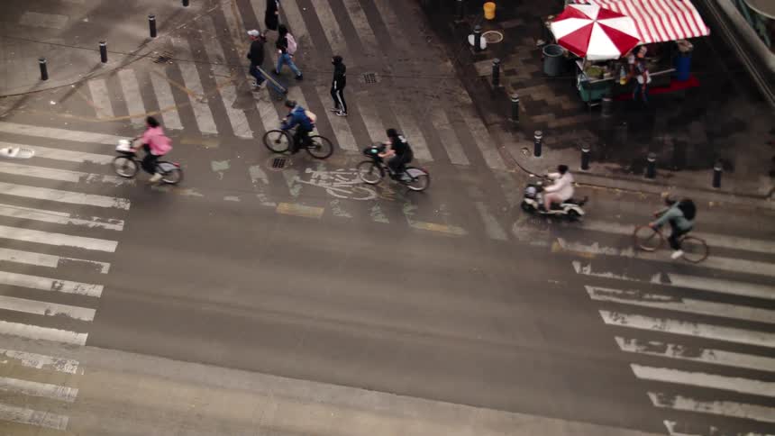 A crowd of people ride bicycles through an intersection in a neighborhood