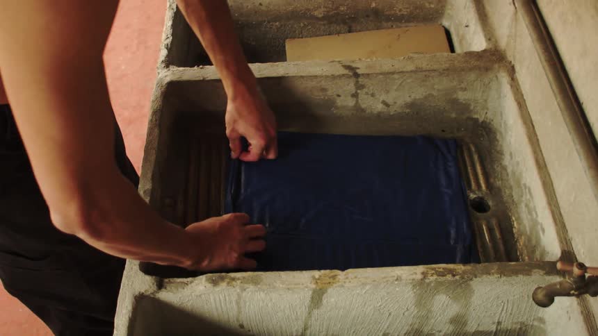A shirtless man washing a clothes item in a wash tank