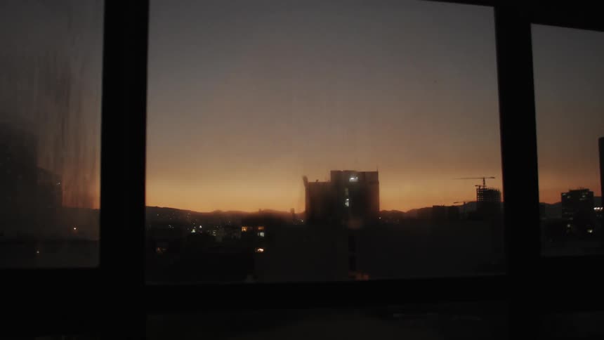 A view of a building through a glass window and the sky is orange due to the morning