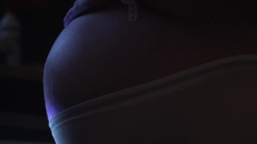 The belly of a pregnant woman her hand caressing it as she rocks back and forth