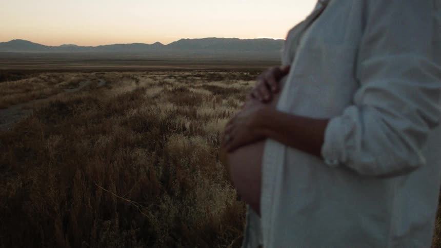 A pregnant woman rubs her stomach while outdoors