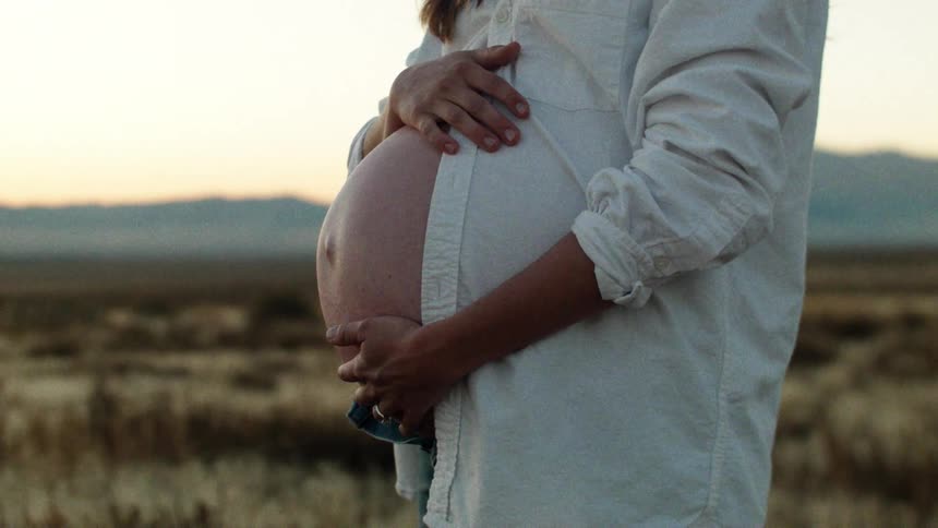 A woman with a large pregnant belly is rubbing her own belly