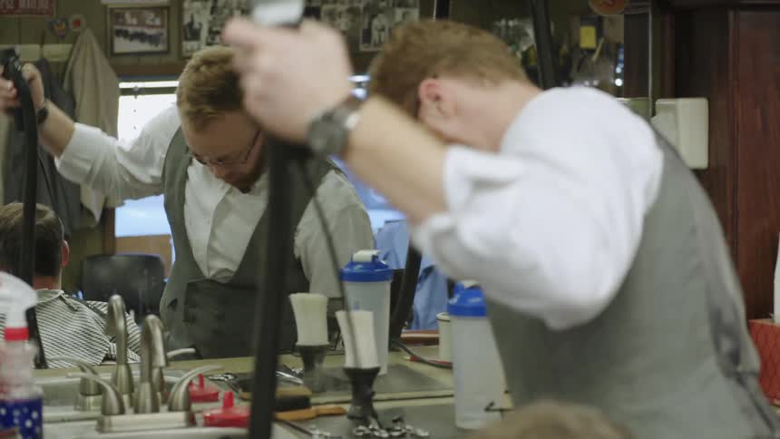 A barber works in his station preparing a razor