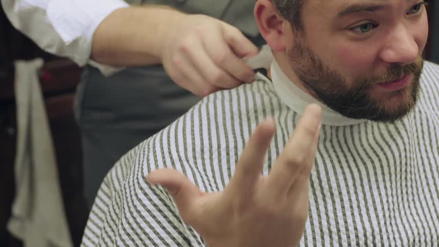 A barber adjust an apron on his customer