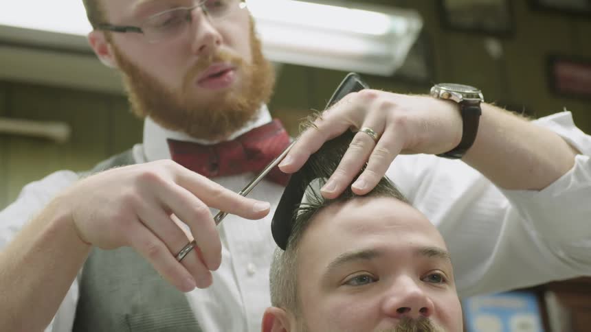 A bearded man trims a customer's hair