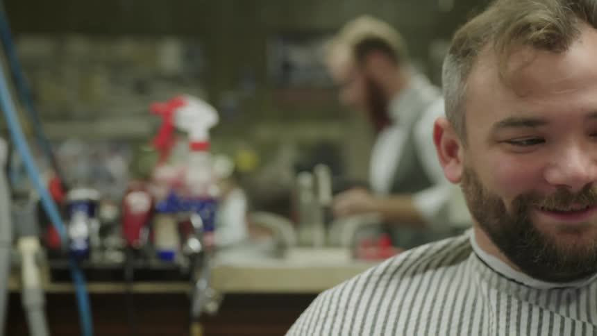A customer sits in a barber chair and talks as his hair is worked on