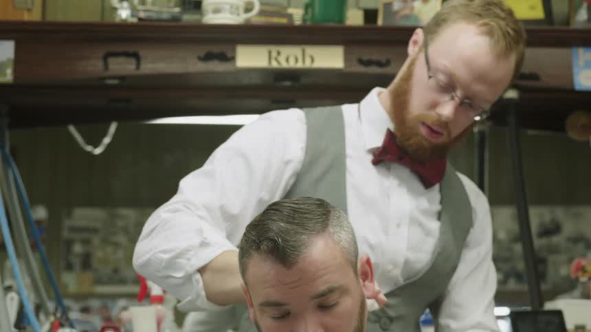 A barber is wiping hair off of a customer