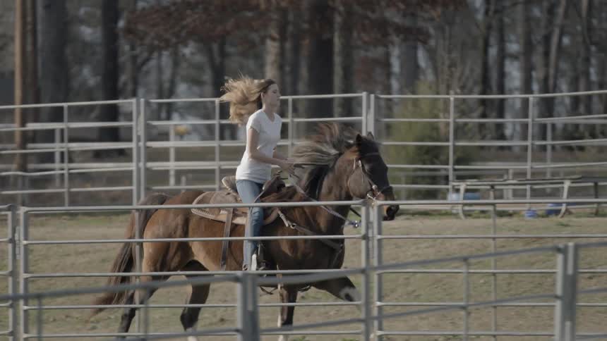A woman rides a horse at a trot outside some pens