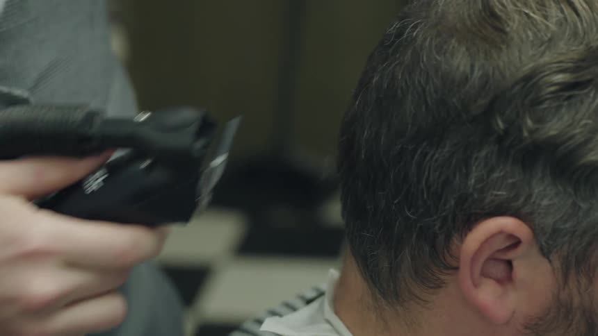A barber is using clippers and a comb on a client's hair