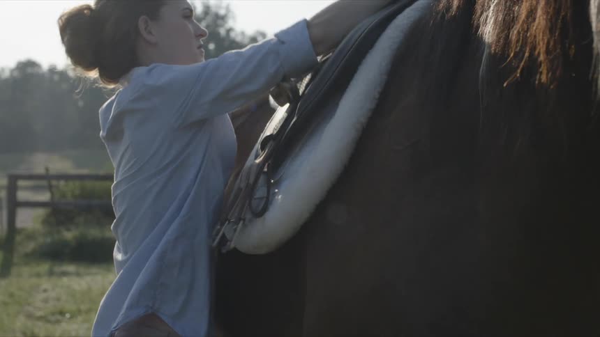 Woman puts a saddle onto a horse's back