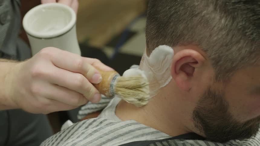 A barber brushes shaving cream onto the customers neck