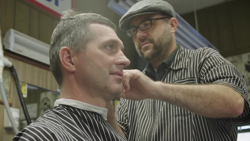 A man is getting his haircut while the barber works and talks