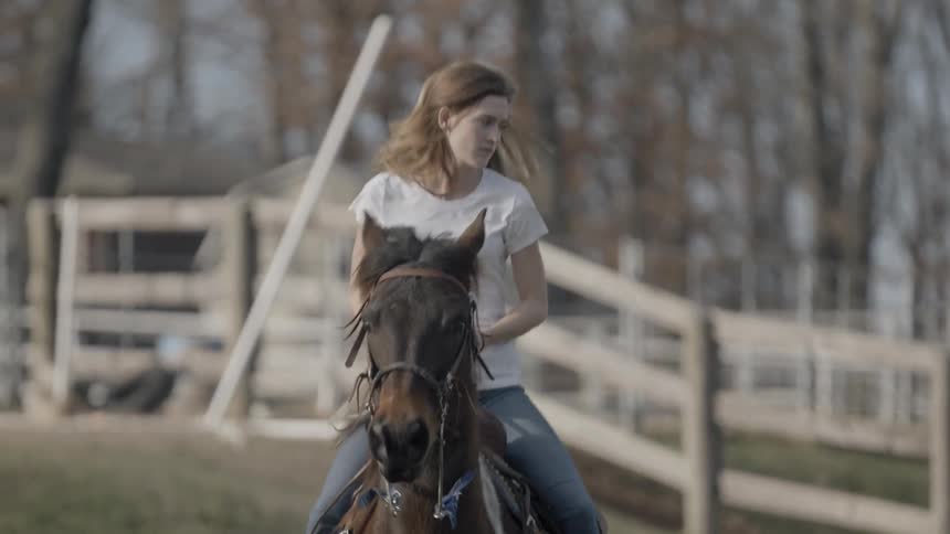 A young woman rides a horse through a field