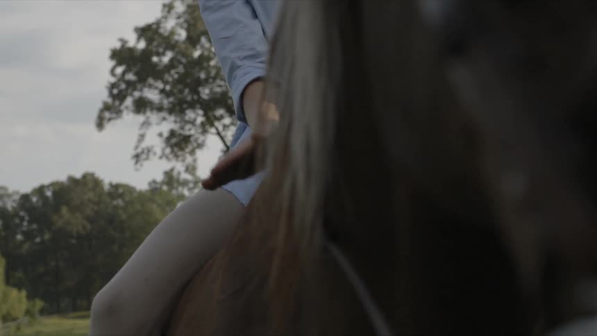 A young woman pets a horse while sitting atop it