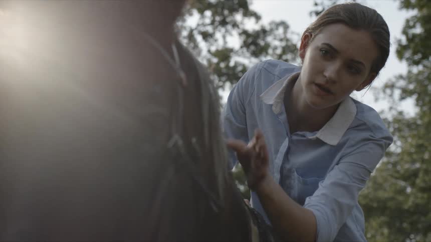 A woman riding a horse reaches over and pats its neck