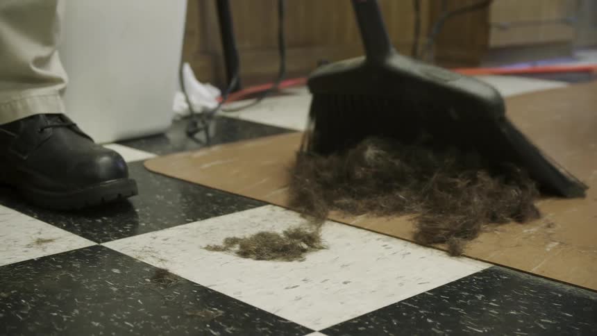 Barber sweeping up hair on the floor into a pile