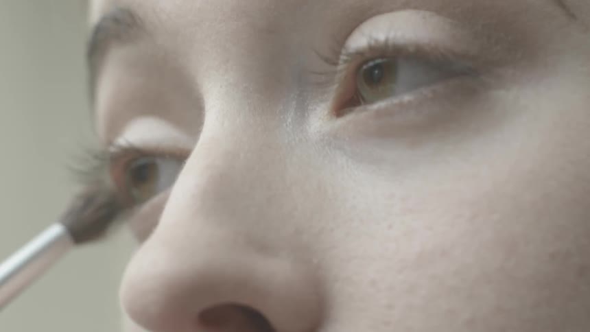 A woman applies eye shadow using a brush