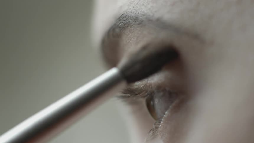A woman is applying makeup above her eyes