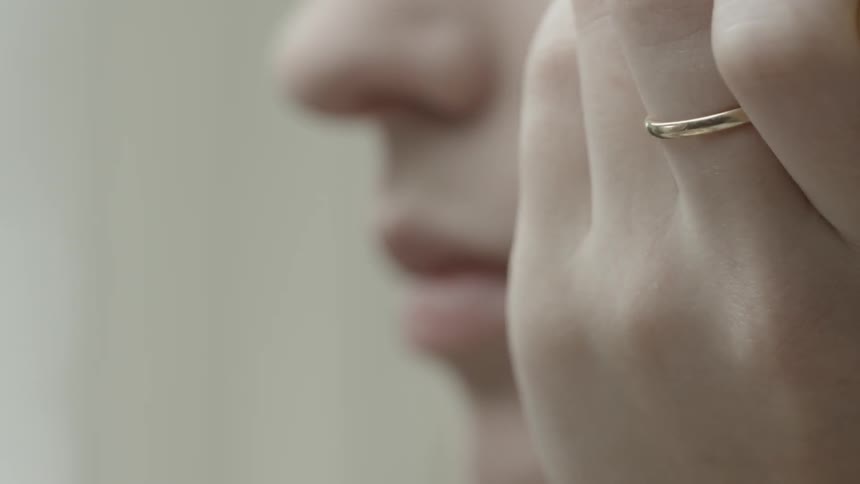 A woman wearing a ring applies makeup to her face