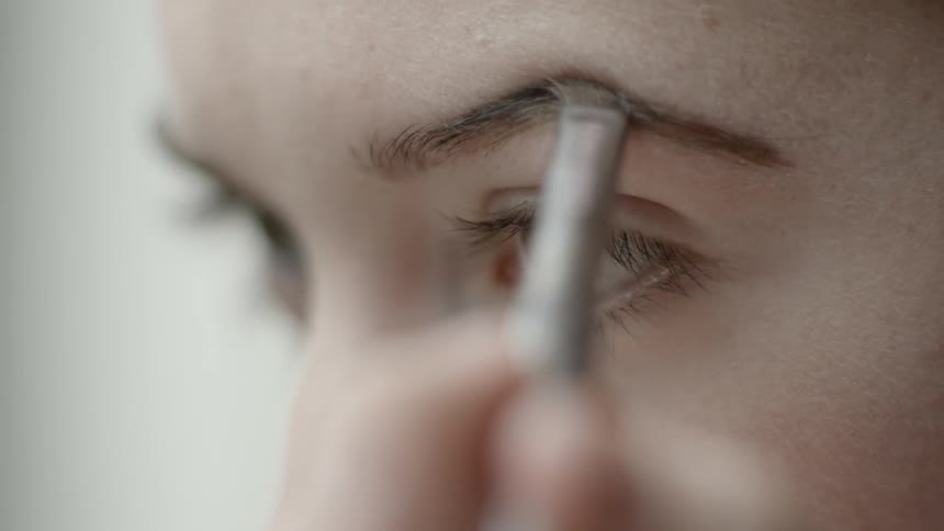 A woman applies makeup to her eyebrows using a brush