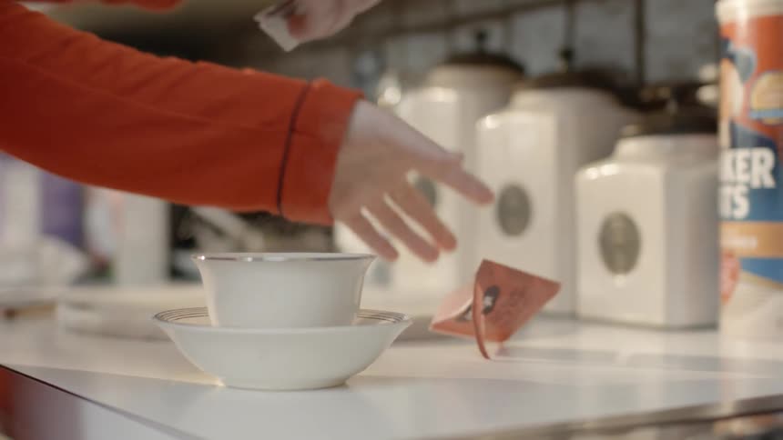 A woman pulls a tea-bag from its package and places it in a cup with hot water