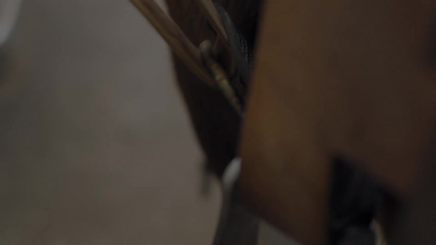 A woman pulls the strap on a horse's saddle to tighten it