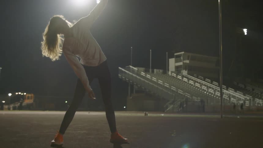 A woman is stretching outdoors at night