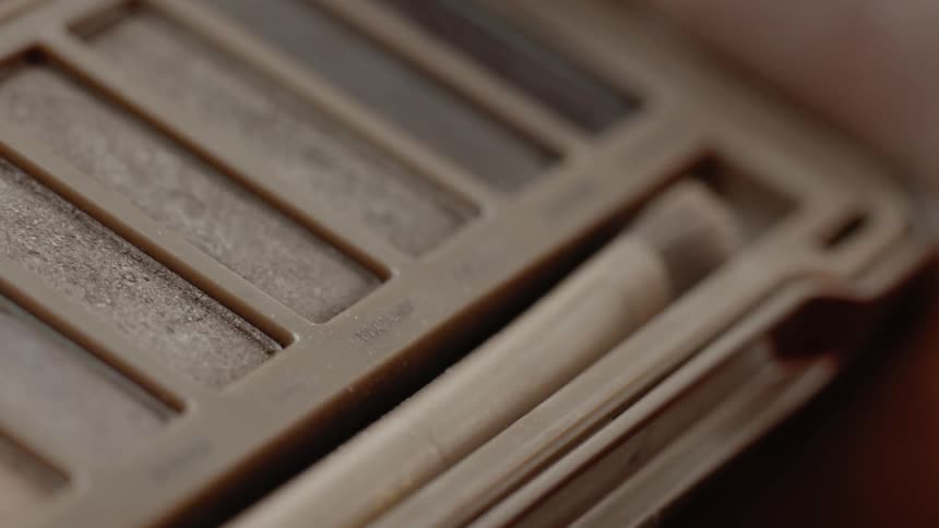 A small brush is dabbed into an eyeshadow palette
