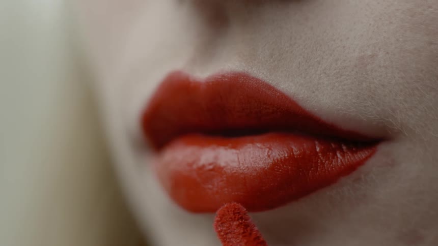 A woman is putting on red lipstick