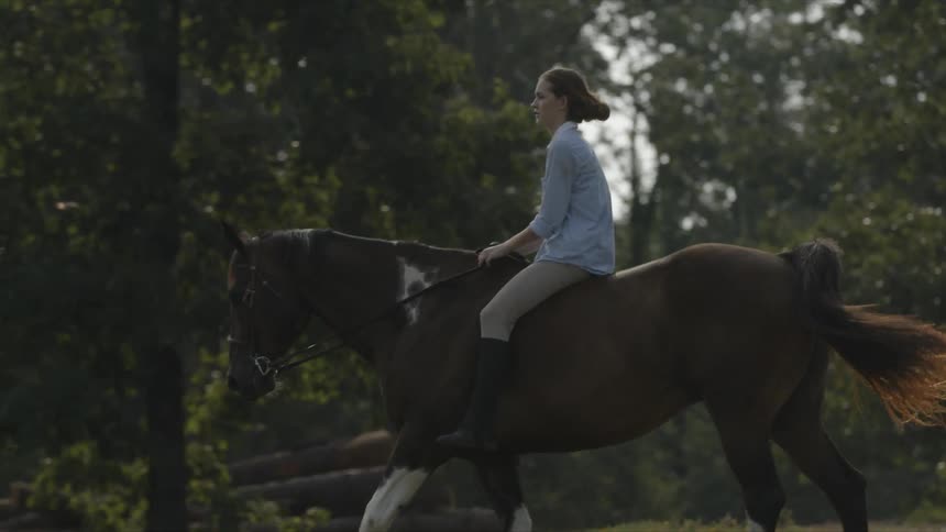 A woman is riding a horse bareback in a field with trees