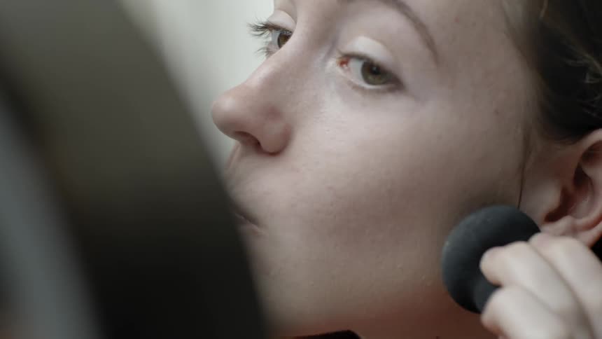A woman is using a sponge to apply foundation to her face