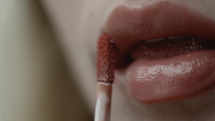 A woman is using a lip wand to apply lipstick