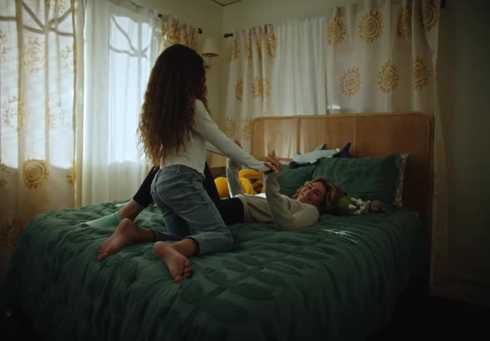 Two girls holding hands laying on a bed