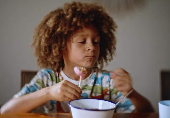 A boy with curly hair eating breakfast with his father