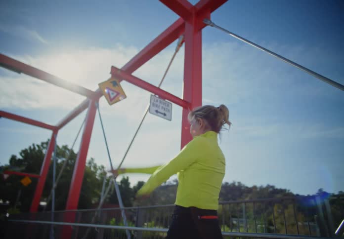 A woman in a yellow shirt is stretching her arms on a street on a bridge