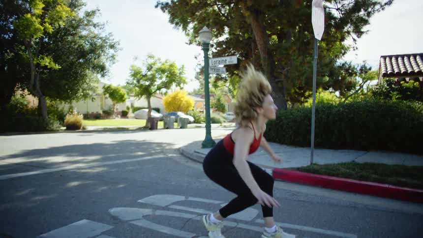 Woman wearing fitness clothes walking on a residential street doing a spin and placing both palms on the ground